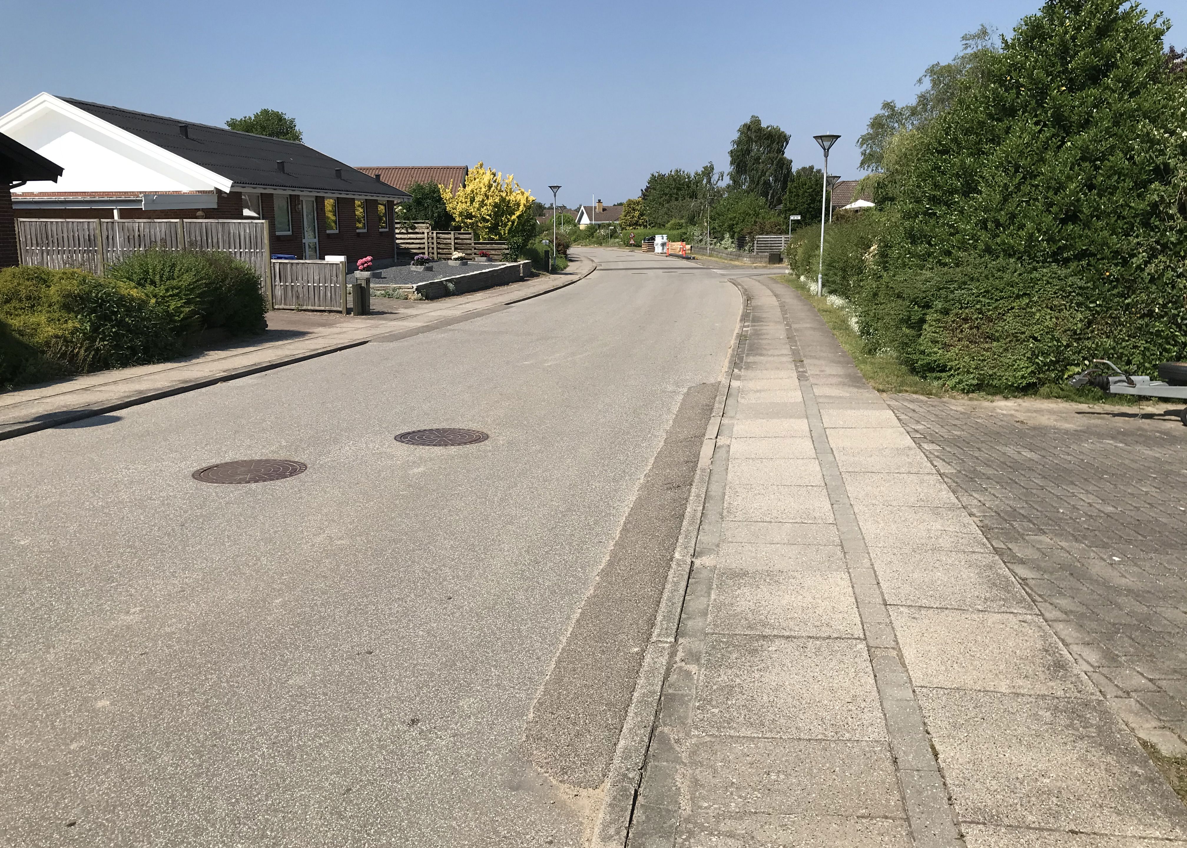Villavej med kørebane og fortov med klassiske fortovsfliser - hækkene er grønne og himlen blå