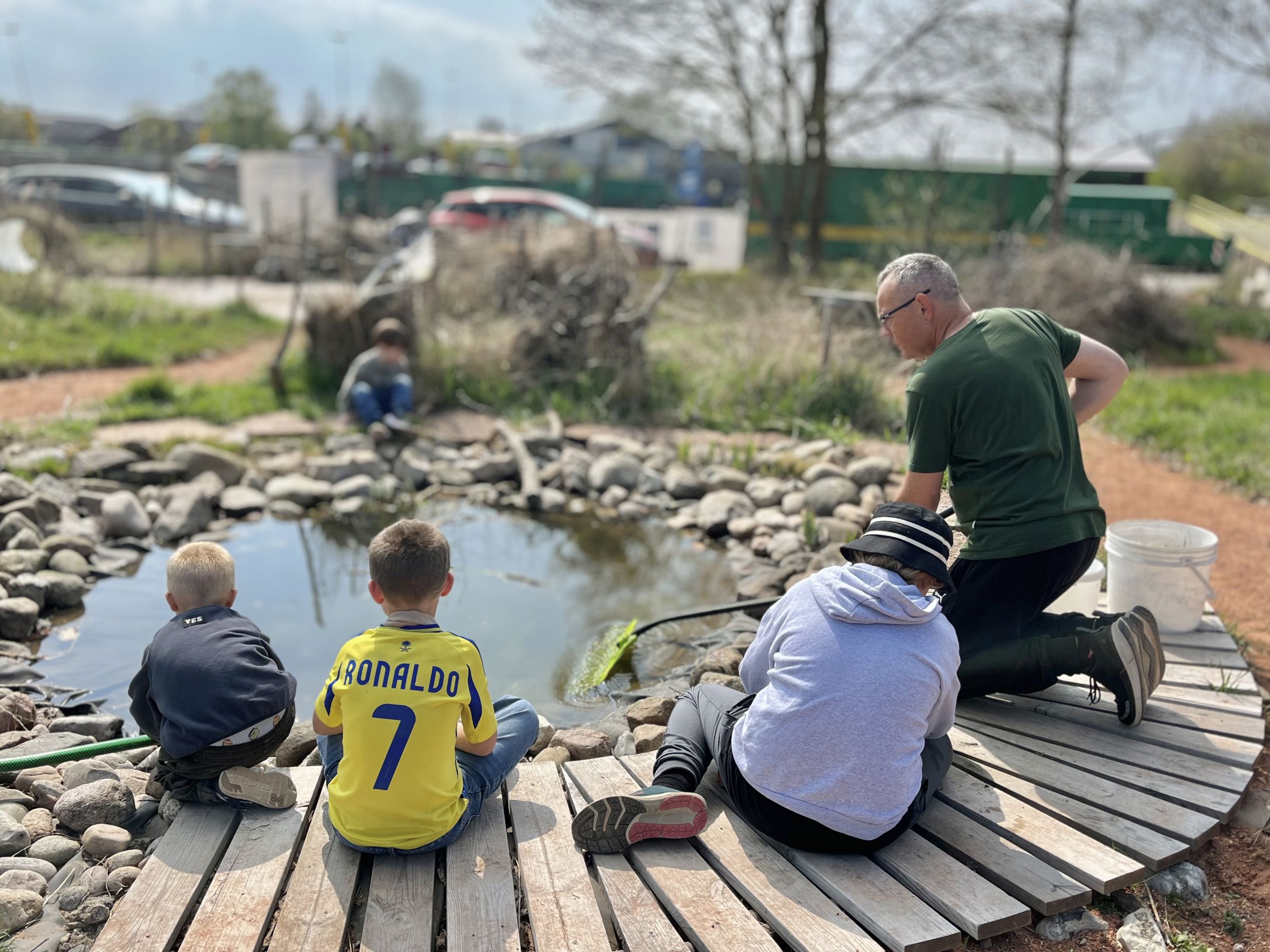 En voksen og flere børn der sidder ved fiskesøen på GenGRO