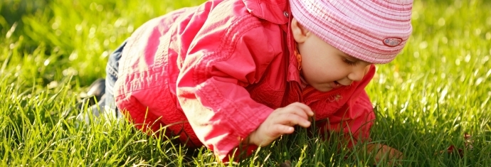 Barn med rød jakke kravler på græsset