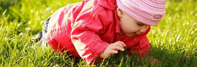 Barn med rød jakke kravler på græsset