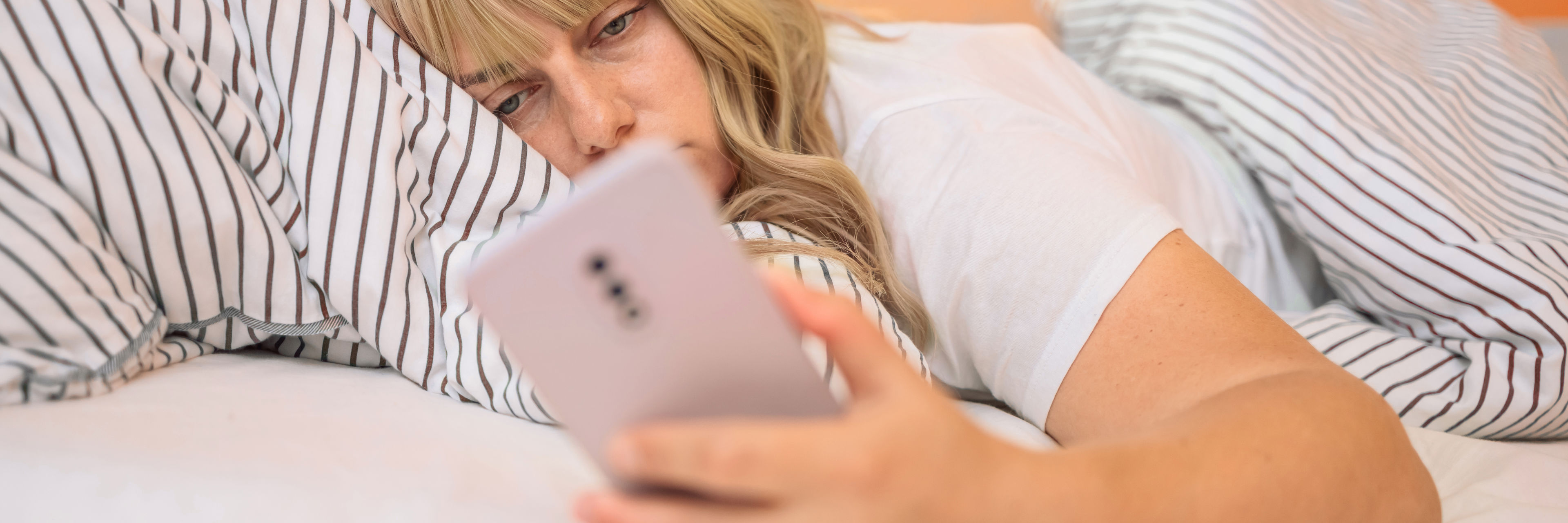 Kvinder der ligger i sengen og kigger på telefonen, fordi hun ikke kan sove grundet stress