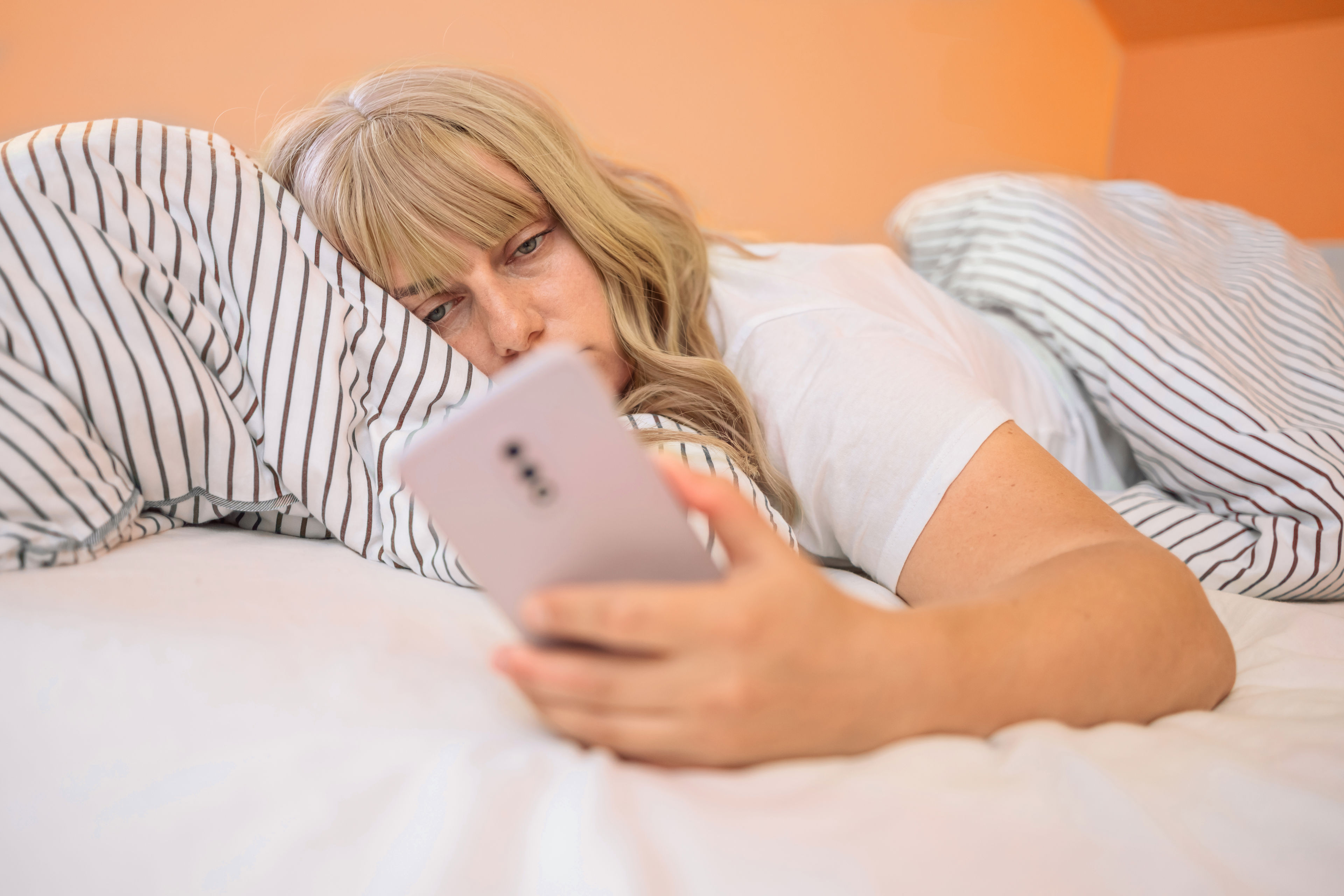 Kvinder der ligger i sengen og kigger på telefonen, fordi hun ikke kan sove grundet stress