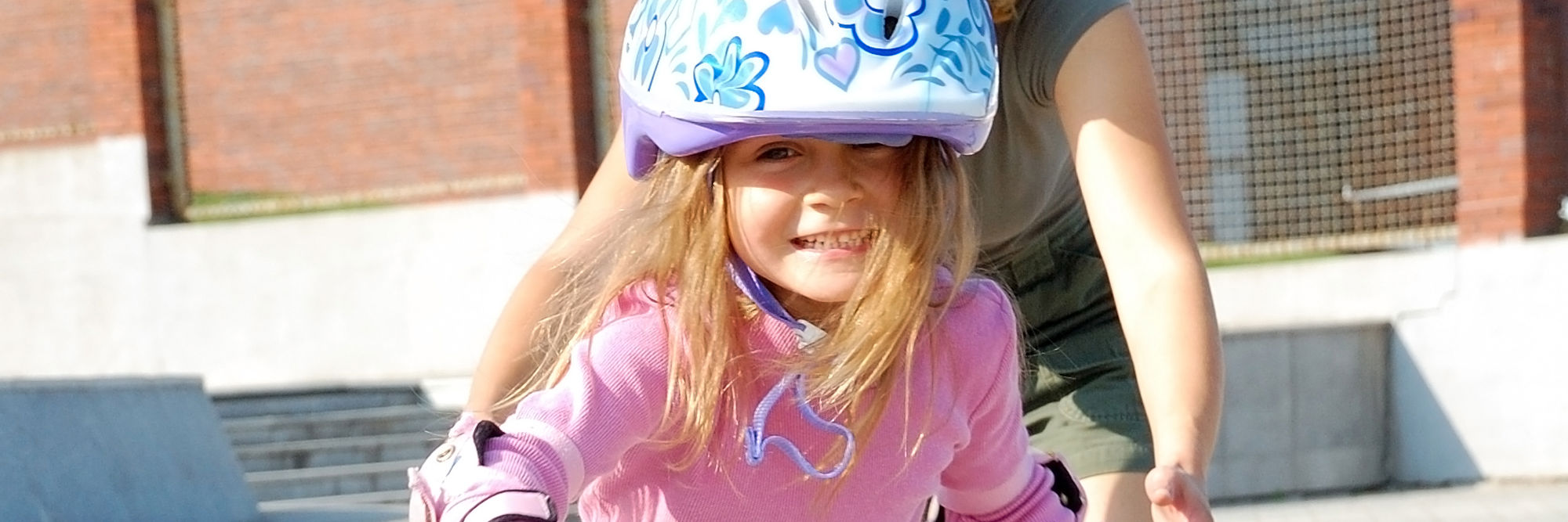 En voksen, der hjælper et barn, der står på rulleskøjter. Alle smiler.