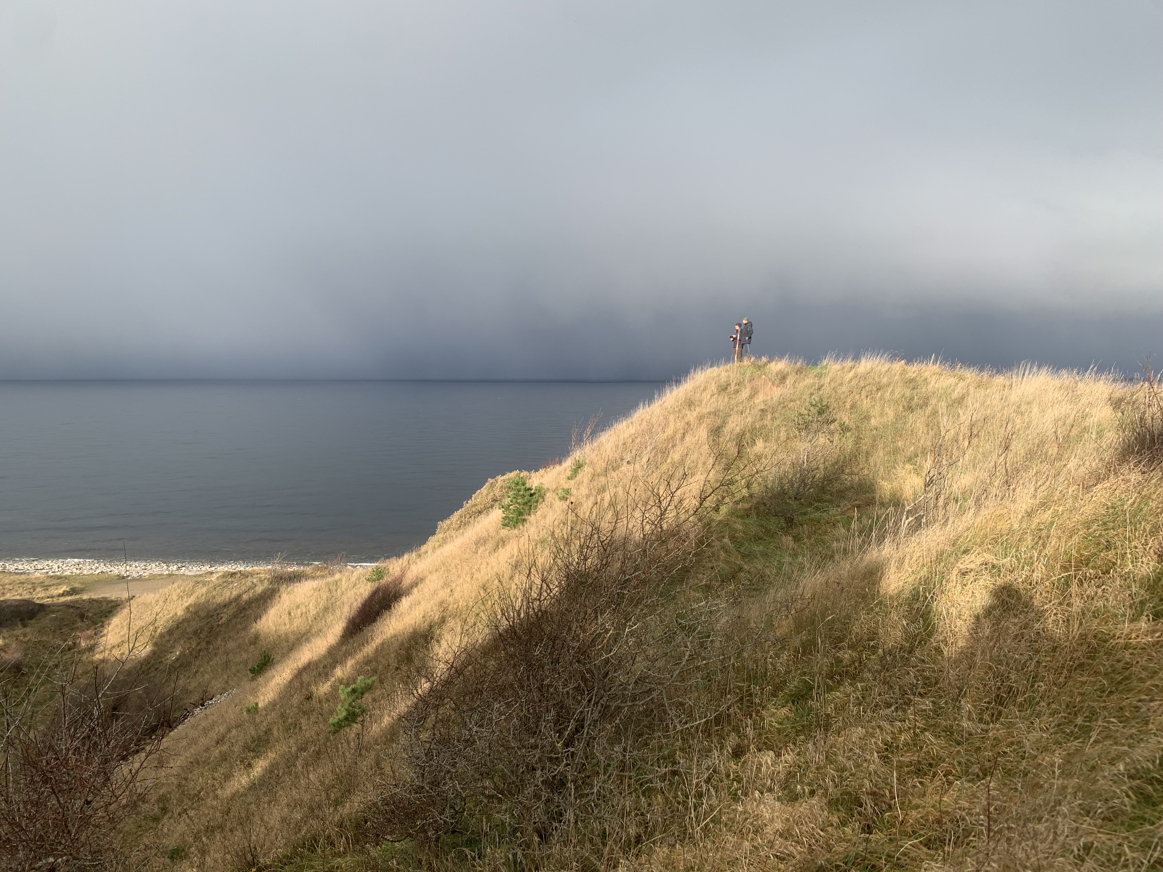 To mennesker på tommen af Klintebjerg på en solrig dag med havet baggrunden