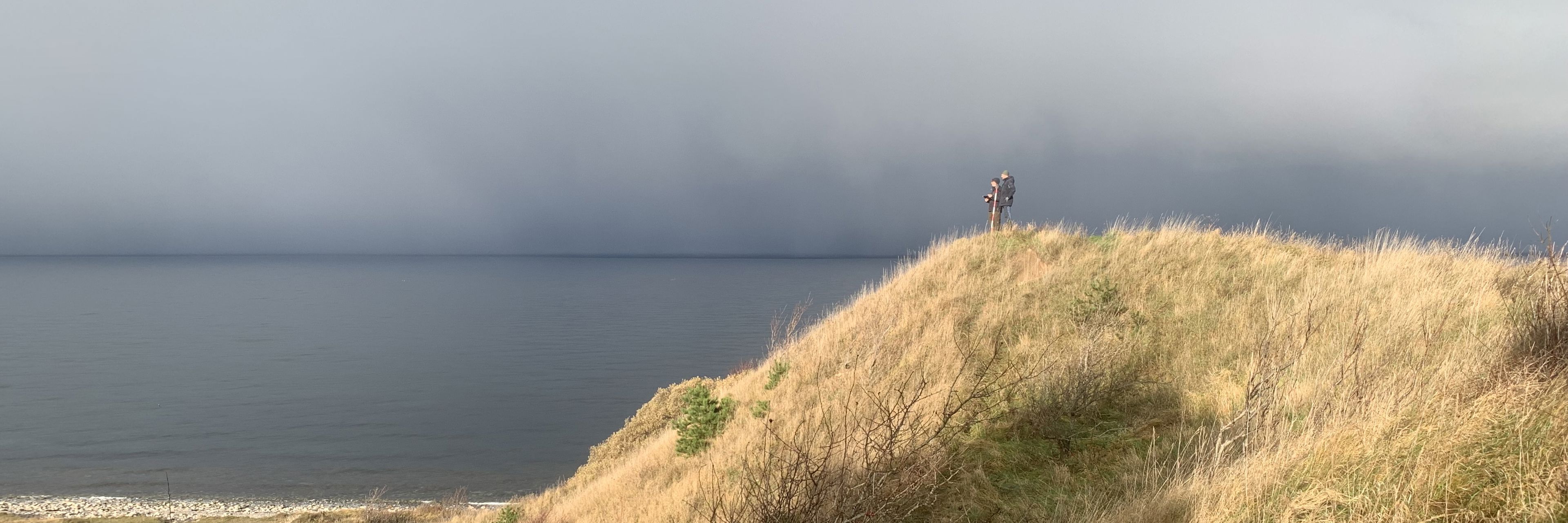 To mennesker på tommen af Klintebjerg på en solrig dag med havet baggrunden