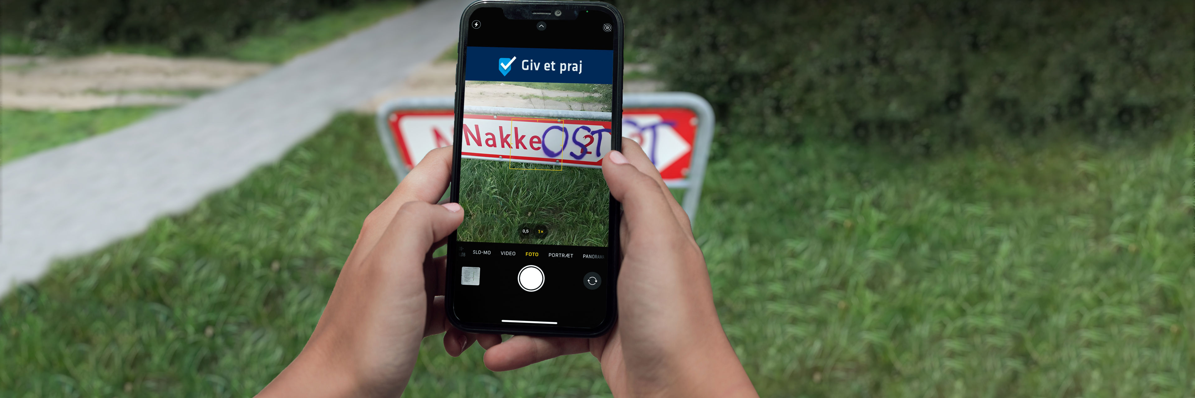 Hænder holder mobiltelefon og tager et billede af et vejskilt hvor der står "Nakke" med henblik på at praje kommunen om graffiti. Ukendte geningsmænd har tilføjet ordet "OST" med graffiti