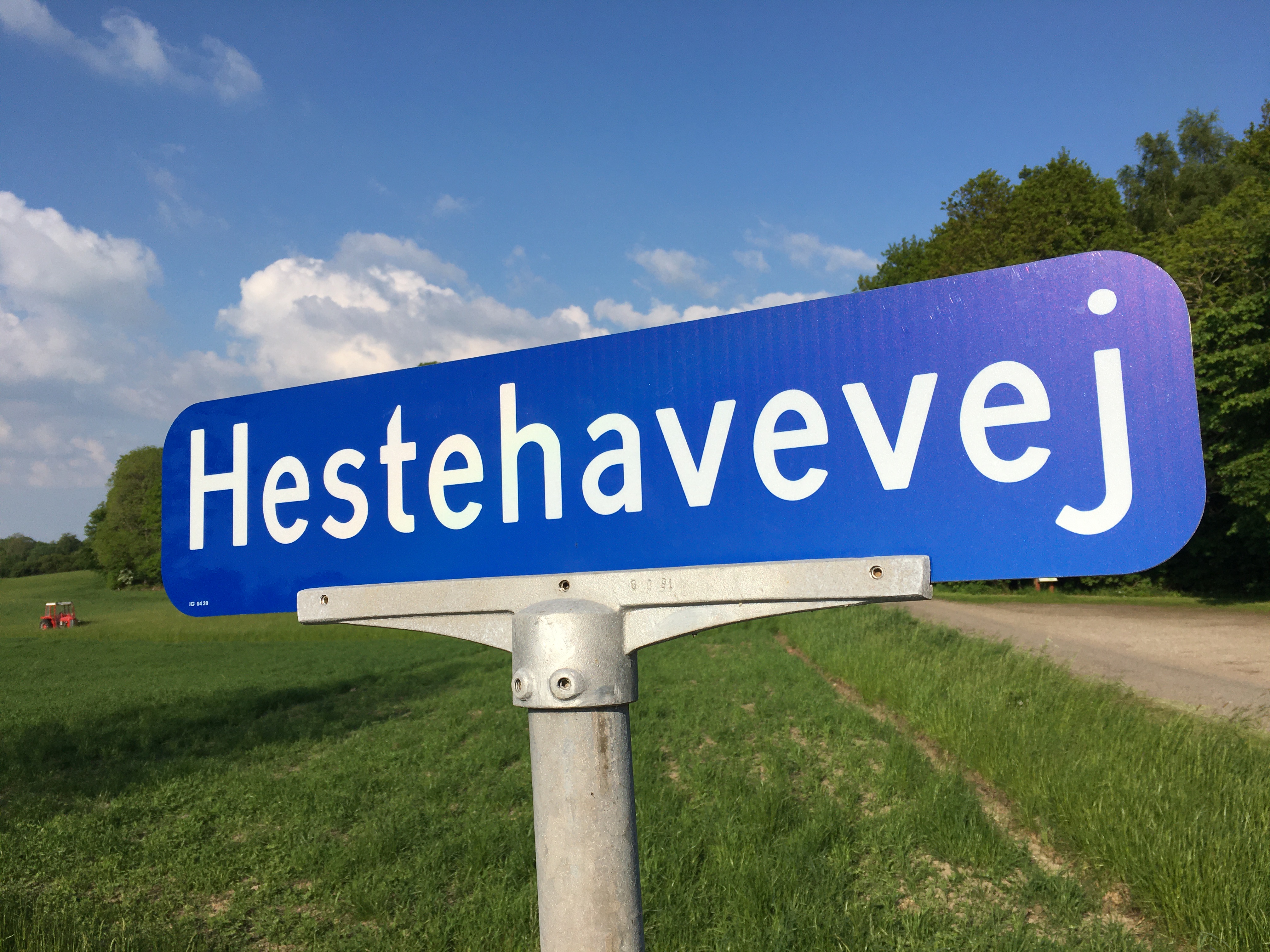 Blåt vejskilt med vejnavnet "Hestehavevej" - i baggrunden ses en mark med en lille rød traktor